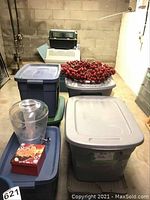 Wide view of plastic storage bins and red berry wreath on top, plastic beverage dispenser with spigot visible, and National Lampoon moose mugs partially seen in background.