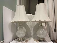 Pair of vintage lamps showing white ribbed glass bases, cream fabric shades with scalloped edges, placed side by side.