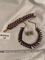 Photo of full jewelry set including purple link bracelet, purple link necklace with gold-tone chain, and gold-tone floral clip-on earrings with blue stones.