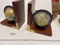 Pair of wooden L-shaped bookends with mounted globes, brass corner protectors, and degree markings on the globes. Measurement scale visible showing size as about 6 inches square.