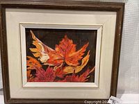 Full view of framed oil painting depicting red and orange autumn leaves on a dark background.