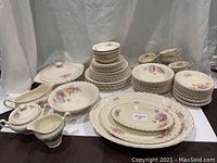 Full set arranged on white surface showing plates, bowls, covered dishes, tea cups, and other serving pieces, highlighting floral pattern and scalloped edges.