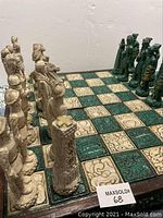 Diagonal view of carved beige and green chess pieces arranged on the carved wood chess board with green and beige inlay squares.