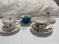 Four tea cups each with matching saucers, floral patterns and gold trim, arranged on white surface