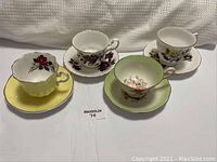 Four vintage teacups each placed on matching saucers, shown from side and angled view to highlight floral patterns and gold trim.