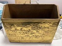 Front view of kindling box showing brass embossed panel with horse-drawn carriage motif.