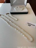 Pearl necklace laid flat next to earring in a box showing overall lot contents.