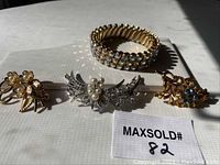 Photo of 3 vintage style brooches with rhinestones and pearls alongside a stretch bracelet featuring aurora borealis rhinestones.