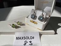 Both pairs of earrings shown: peridot earrings laying down and aquamarine earrings displayed in a white box.