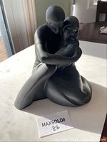 Front view of the black-grey toned figurine showing the man and woman embracing a baby.