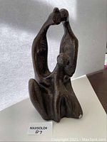 Overall view of the abstract bronze sculpture showing three intertwined figures on a flat surface.