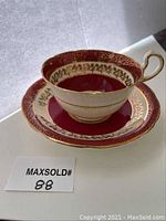 Side and front angle showing the tea cup and saucer with red base color and gold leaf detail against white background.