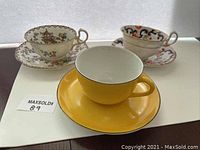 Three china cups with matching saucers, one yellow, two floral patterns.