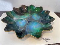 Front view of the large hand painted bowl showing glossy multicolor paint swirl in green, blue and black tones with gold trim and wavy edges.