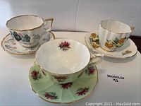 Front view of all three china tea cups and their matching saucers showing distinct floral patterns and gold trim.