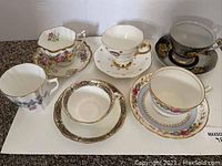 Overview photo of six ceramic tea cups and matching saucers with various floral designs and gold trim.