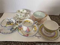 Front view of five assorted bone china cups and saucers arranged in a row showing pattern and cup shapes.