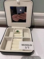 Cream travel jewelry case open, showing ring in center compartment and built-in mirror