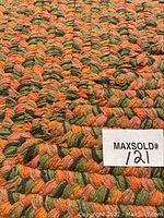 Close-up showing braided textile pattern with orange, green, and beige yarns intertwined.