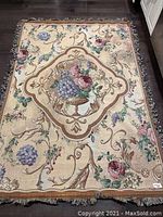 Full view of the rectangular floral tapestry with wooden edges visible on the bottom side, displayed on dark flooring.