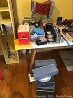 Full view of table with Burke and James 5x7 view camera with red bellows, camera case, film developing tanks, reels, slide viewer, and assorted accessories.