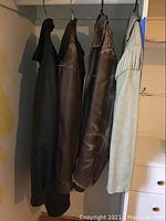 Four men's leather jackets hanging on a rack including three brownish shades and one light beige jacket with fringe.