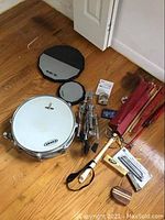 Photo of drum, practice pads, drumsticks, drum stand, wooden mallet, and other percussion accessories on floor.