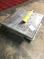 Tile saw with flat metal table surface showing grooves and cuts, grey metal body, yellow blade guard.