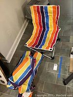 Front view of one folded beach chair and two matching carrying bags on tiled floor.