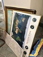 Framed posters and maps leaning against a wall including the 'The Living Earth' world map and other framed art with various sizes