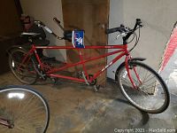 Full side view of red tandem bicycle showing overall frame, seats, handlebars and wheels