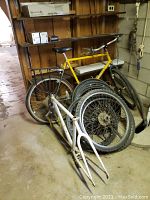 Yellow Univega bicycle, white Raleigh frame, stack of rims and tires in basement setting