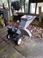 Side angle view showing entire chipper shredder with dirt and leaves around, wheels visible.