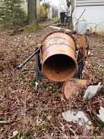 Side view of the orange concrete mixer drum, showing rust, dirt, and outdoor debris inside and around it on the ground with leaves and twigs.