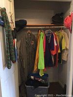 Closet view with hanging clothes including the vintage Esso coverall, various jackets, and plastic bin on floor.