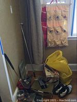 Photo showing fabric organizers hanging on wall in cream and red fabric with embroidered golf players, corner of room with golf-related items on floor including golf clubs, shoes, bags, boxes.