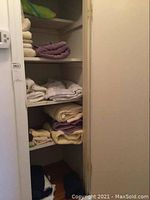 Shelved linens including folded towels, sheets, and mattress cover in assortment of colors including white, cream, and purple.