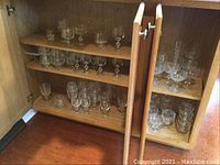 Wooden cabinet with multiple shelves holding a variety of clear stemmed glasses in different shapes and sizes.