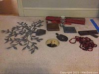 Photo showing three vintage red wooden levels, a metal iron stand, paper cutter, glass jar with pins, locks, a photograph, beads, and a vintage molding plane.