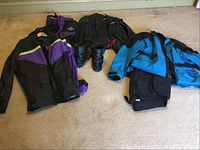 Photo shows multiple motorcycle jackets in purple, black, and blue colors laid out with boots in front.