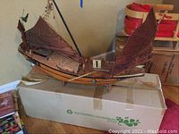 Full side view of Vietnamese junk model ship on cardboard box, showing the overall structure with three brown sails and hull details.
