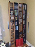 Four Ikea media storage stands in wood and black finishes, arranged side by side against a wall, filled with CDs and DVDs. Red plastic stand in front.
