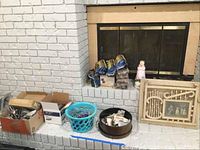 Wide view of lots on floor by fireplace including boxes of flatware, blue basket with shells, silver bowl, Pine Mountain logs, magazine rack, candle holders, and casters.