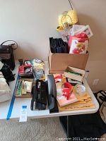 Photo showing assorted office supplies on table including binders, tape dispensers, hole punch, tape rolls, envelopes and gift wrap