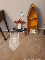 Wide shot showing the boat shelf standing upright, wooden anchor leaning against the wall, crocheted lighthouse banner on the carpet, clock in front of the boat shelf, and miniature wooden houses.