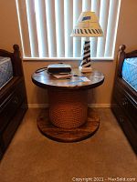 Full view of spool table with lamp and alarm clock on top between two beds.