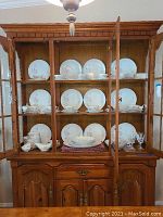 Full china cabinet with 12 place settings of white china with pink rose floral pattern, stemware, and serving pieces displayed