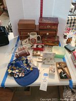 Assortment of three wooden jewelry boxes, enamel pin–covered blue visor, cufflinks, jewelry cases and loose items displayed on table
