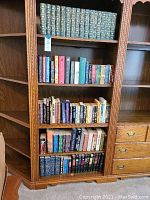 Full bookcase shelf showing mixed volumes of green leather-bound classics and assorted fiction on adjacent shelves