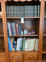 Full bookcase view showing Harvard Classics top shelf, mixed books and bookends second shelf, additional books and stones on third shelf